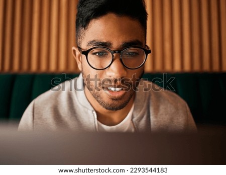 .. Closeup of geeky young indian man wearing glasses while reading something interesting and sitting inside. Man wearing glasses while reading online. Dedicated male student doing research in cafe.