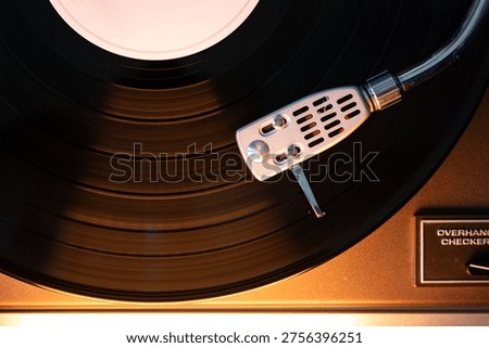 Close-up of a generic silver headshell and needle tracking a black vinyl record. The scene features a warm orange highlight reflecting off the surfaces under ambient indoor lighting Stock photo © 