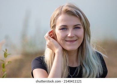 Close-up of a gentle smiling girl with  gray eyes. She has blonde hair and a black T-shirt. Horizontal photo of a cute girl 20 years old on a blurred background of nature. - Powered by Shutterstock