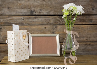 Close-up of gift bag, photo frame and flower vase on wooden surface - Powered by Shutterstock