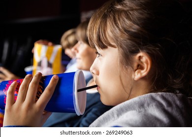 Closeup Of Girl Drinking Cola While Watching Movie With Family In Cinema Theater