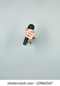 Close-up Of Girl Hand Holding A Black Microphone Through A Torn Grey Paper