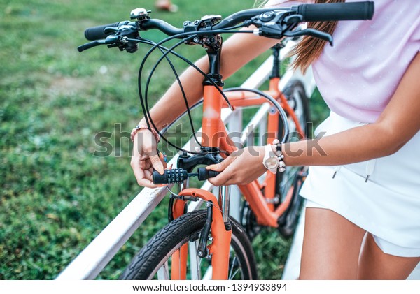 Close-up girl hand lock with digital cipher.\
Woman summer stands bicycle locking bicycle with cable. Picks\
password lock theft bicycle parking lot. Bicycle rentals Cycling\
weekend. Active\
lifestyle.