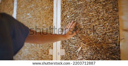 Close-up of girl hand touching straw wooden eco house framing. Concept of sustainability and healthy living.
