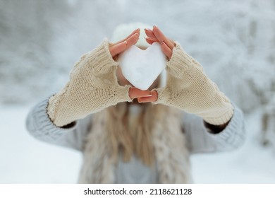 Close-up girl holds a snowy heart in front of her in gloves