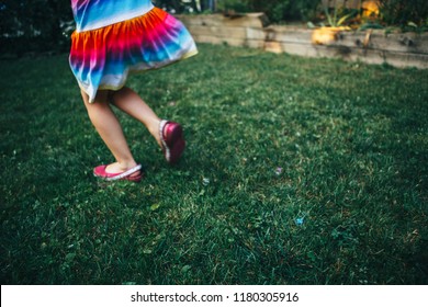 Closeup Of Girl Legs On Grass. Child In Colorful Dress Running In Garden On Home Backyard. Real Authentic Happy Childhood Moment. Soap Bubbles On Ground. Toned With Film Filters. 