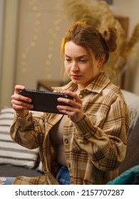 Close-up. The girl is sitting in the room on the sofa with a portable game console in her hands. Video games, mobile games, entertainment, game strategy, youth culture.