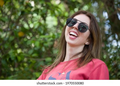 Closeup of girl smiling with aviator sunglasses and red jumper in a park garden outdoors