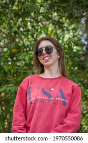 Closeup of girl smiling wearing sunglasses and red jumper in a park garden outdoors
