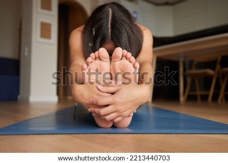 Close-up of a girl stretching to touch her toes while sitting on a yoga mat.