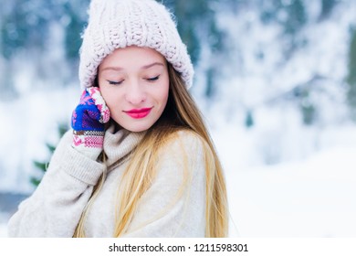 Close-up of a girl's face in a sweater and a hat that closed her eyes against the background of snow and wood