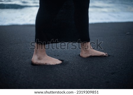 Close-up of a girl's feet walking on a beach with black sand
