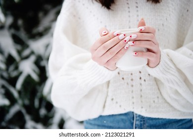 Close-up of girls hands with Valentine day manicure white color with red hearts holding cup of coffee outside on winter day