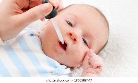 Closeup of giving vaccine to newborn baby boy from eyedropper or syringe. Concept of babies and newborn vaccination and giving vitamins. Caring parents with little children