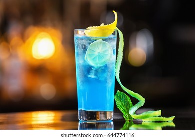 Closeup glass of blue lagoon cocktail decorated with lime at festive bar counter background.