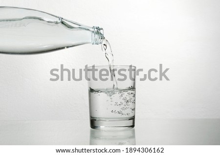 Closeup of glass bottle and glass full of fresh water.Pouring cold water from glass bottle into the glass cup against bright background