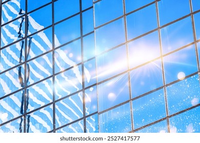 A close-up of a glass facade reflecting the blue sky and white clouds, with a sun flare shining through. - Powered by Shutterstock