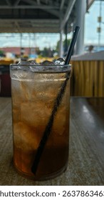 A close-up of a glass filled with iced tea and a black straw, showing condensation and ice cubes, taken at an outdoor cafe with blurred background for a fresh and chill mood.