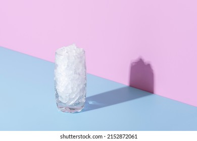 Close-up with a glass full of crushed ice, isolated on a blue background. Glass with ice in bright light against colorful background.