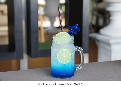 Closeup Glass Of Iced Blue Hawaii Soda With Lemon On Table And On Blurred Background, Summer Cocktail Or Tropical Mocktail.