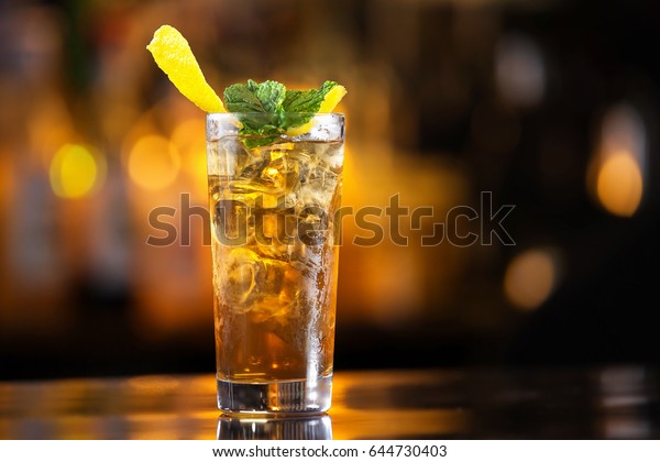 Closeup glass of long island ice tea\
cocktail decorated with mint at bar counter\
background.