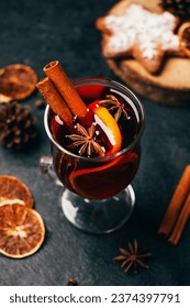 close-up of a glass with mulled wine cinnamon and cardamom on a black background with ingredients for the drink