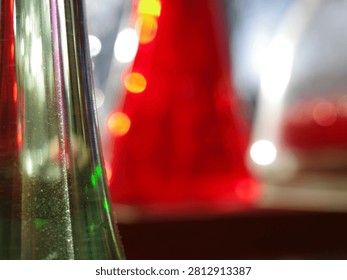 Close-up of glass objects with blurred background. Foreground features a transparent green glass surface with visible texture, reflecting light. Background shows blurred red and white glass objects. The image creates an abstract composition, emphasizing the play of light and color on and through the glass. 