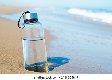 крупный план стеклянной бутылки с водой многоразового использования на берегу моря одинокого пляжа