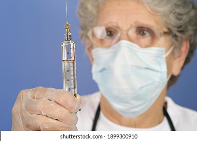 Close-up glass syringe with a large needle filled with drug solution for injection. With senior female doctor in background