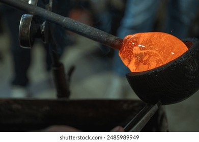 Close-up of a glassblower shaping hot molten glass under a high fire in a workshop. Manual processing of glass by masters inside the glass. Selective focus - Powered by Shutterstock