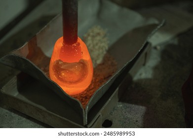 Close-up of a glassblower shaping hot molten glass under a high fire in a workshop. Manual processing of glass by masters inside the glass. Selective focus - Powered by Shutterstock