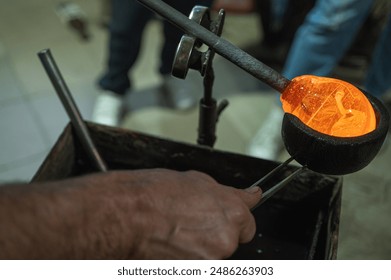 Close-up of a glassblower shaping hot molten glass under a high fire in a workshop. Manual processing of glass by masters inside the glass. Selective focus - Powered by Shutterstock