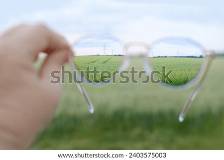 closeup glasses in female hands, wheat field in lenses, cleanliness and transparency of lenses, concept of harvest of bread, eyewear accessories, food crisis, lens care products, clear optics