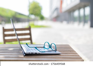 Close-up Of Glasses And Laptop On A Wooden Table Of A Summer Cafe. Freelancer Workplace. Remote Workplace. No People.