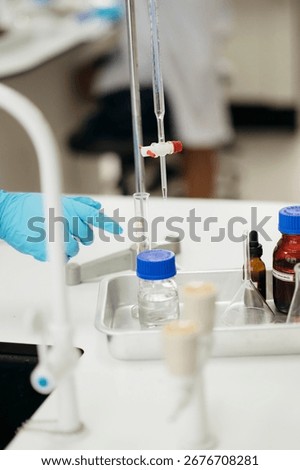 Close-up of a gloved hand in a laboratory using burette and beakers during chemical experiment, research, or educational demonstration