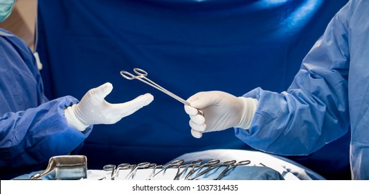 Close-up of gloved hands holding surgical scissors.Medical team performing operation,Group of surgeon is working in operating theater toned in blue,surgical team in operating theater, 