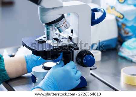 Closeup gloved hands operating microscope, unspecified technician performing clinical sample analysis on glass slide,