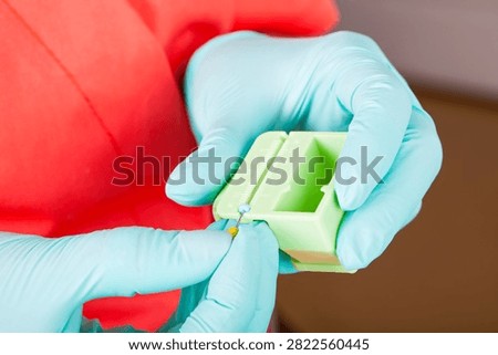 Close-up of gloved hands setting the precise working length of an endodontic file with a rubber stopper and millimeter measuring block.