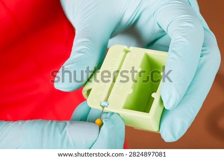 Close-up of gloved hands setting the precise working length of an endodontic file with a rubber stopper and millimeter measuring block.