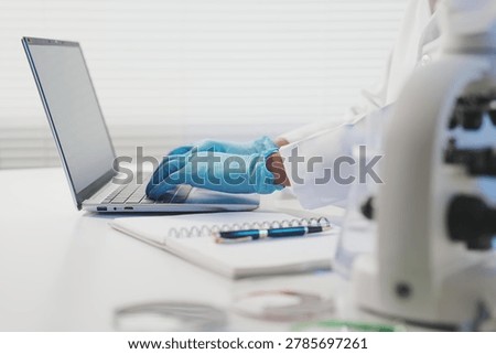 A close-up of a researcher’s gloved hands typing on a laptop keyboard next to a notebook and lab equipment, symbolizing the transition from physical experimentation to digital data analysis.