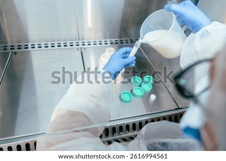 Close-up of gloved hands using measuring jug to fill sterile syringe with donor breast milk for accurate administration in neonatal care facility.