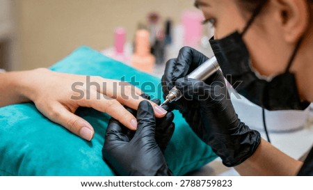 Close-up of a gloved technician using an electric file to shape a client's fingernail in a salon setting with blurred background