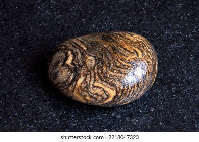 Close-up of gneiss pebble on dark granite polished slab. Beautiful texture of striped stone. Selective focus. - Shutterstock ID 2218047323