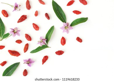 Closeup Of Goji Berries, Lycium Barbarum. Dried Asian Fruit, Leaves And Blossoms Isolated On White Wooden Background. Healthy Superfood. Floral Pattern, Decorative Corner. Flatlay, Top View.  