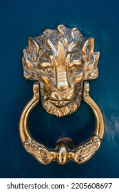 Closeup Of A Gold Door Knocker On A Blue Door. A Metallic Lion Head To Knock And Open The Door. Antique On The Door Of A Wealthy Neighborhood.