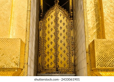 Close-up of the gold mosaic tiles and decorative door of Phra Si Rattana Chedi: a gold bell-shaped stupa at the Wat Phra Kaew (Temple of the Emerald Buddha) inside the Grand Palace - Bangkok, Thailand