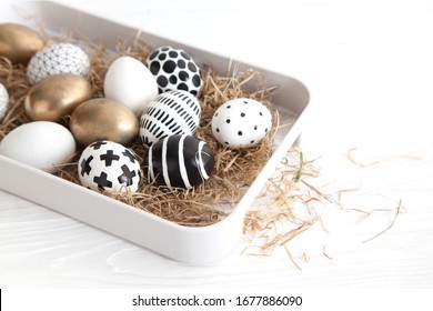 Close-up of golden and black and white minimalist painted easter eggs lie in the hay on a white tray with sides on a white table. Stylish modern rustic easter concept. Copyspace - Powered by Shutterstock