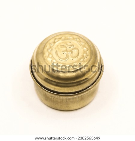 closeup of a golden bronze box jar with hindu om symbol inscribed on the crafted lid isolated in a white background