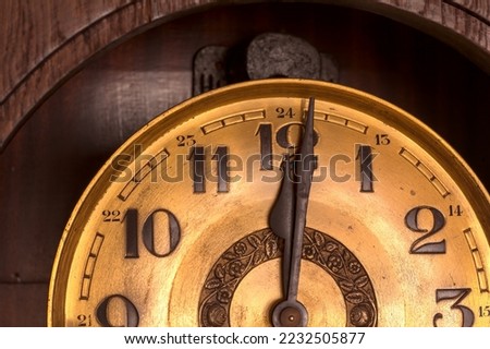 Close-up of the golden face of an old clock showing twelve o'clock (noon, midnight).