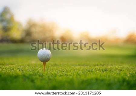Close-up golf ball on tee with fairway golf course and sunrise background.